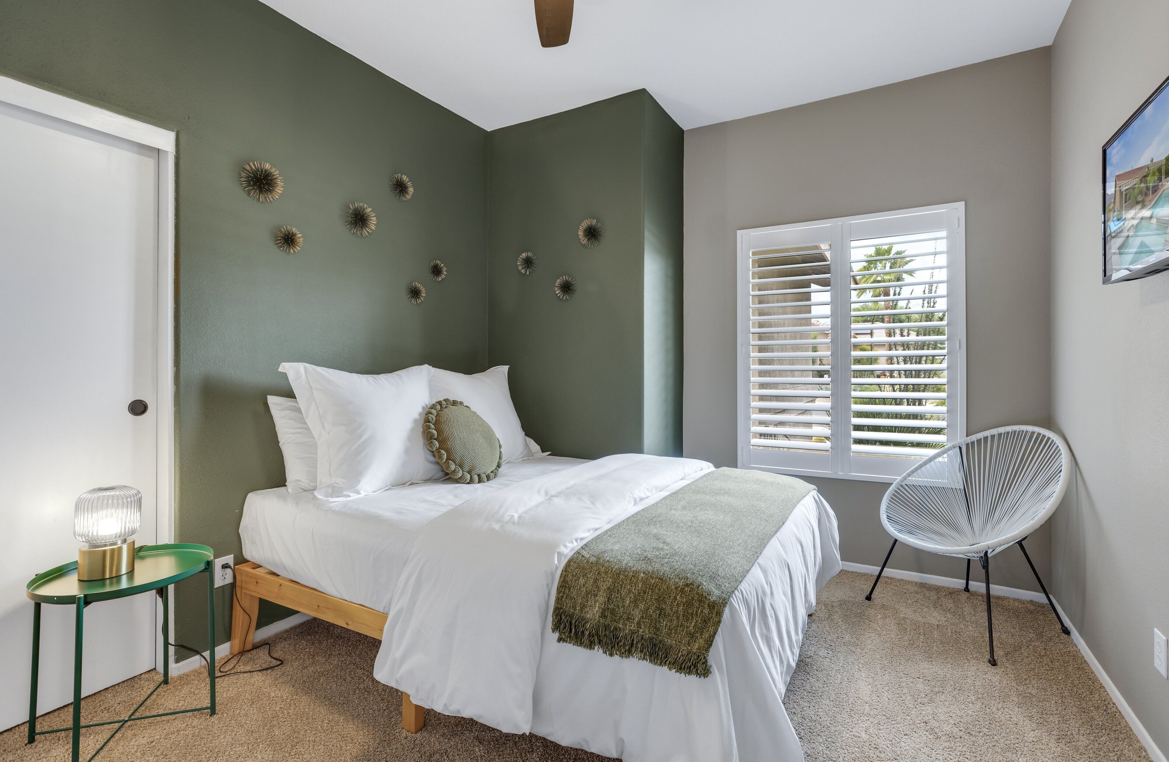 A bedroom with a bed, a chair, a window with blinds, and decorative wall art.