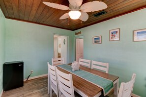 A dining area with a wooden table, white chairs, a ceiling fan, and a refrigerator. - Tropical Retreat, Updated Private Home With Wifi (Ormond Beach)
