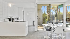 Una cucina moderna con mobili bianchi, un'isola centrale e una zona pranzo con tavolo in vetro e sedie bianche.