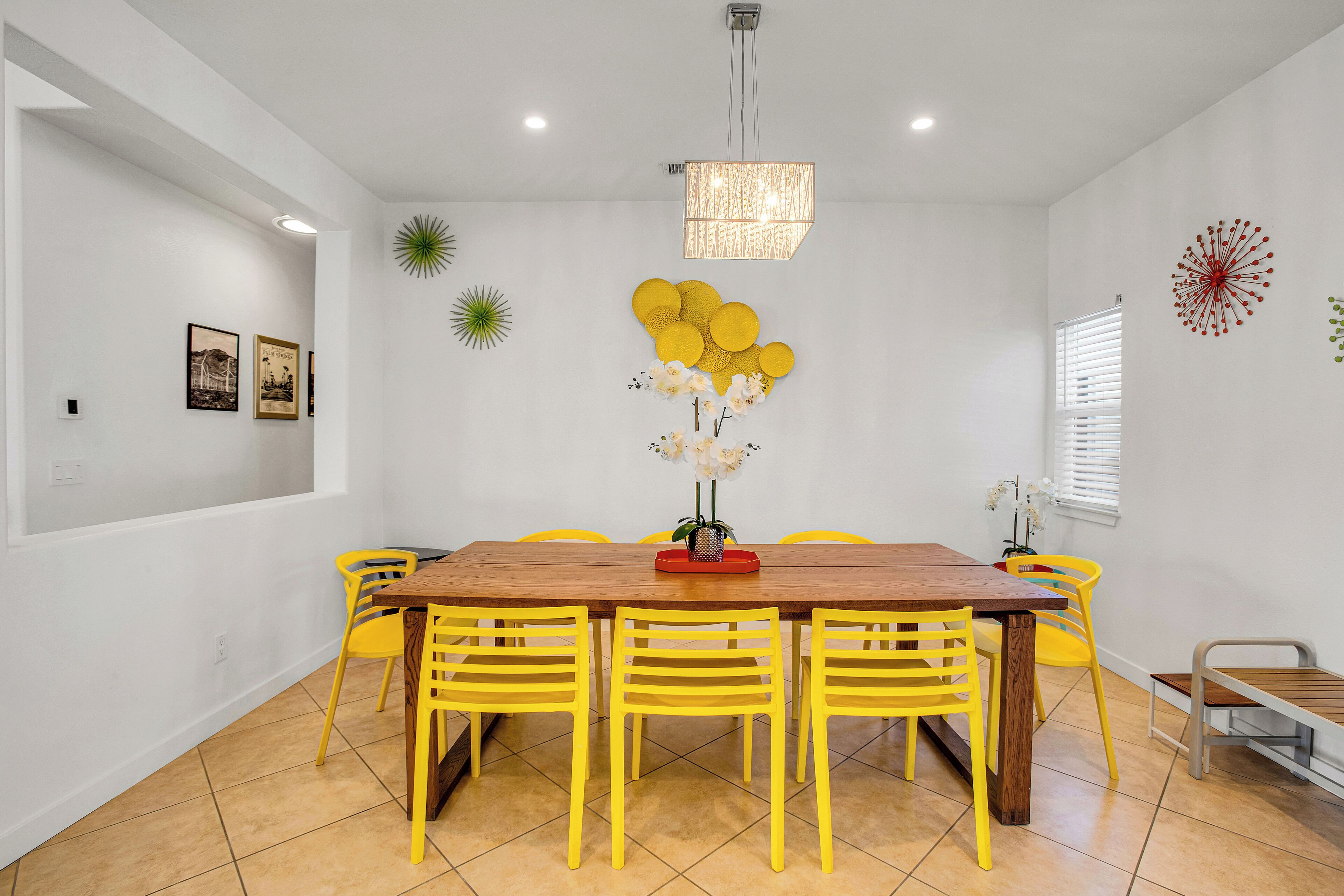 Un espace repas avec une table en bois et des chaises jaunes, un lustre et des éléments décoratifs sur les murs.