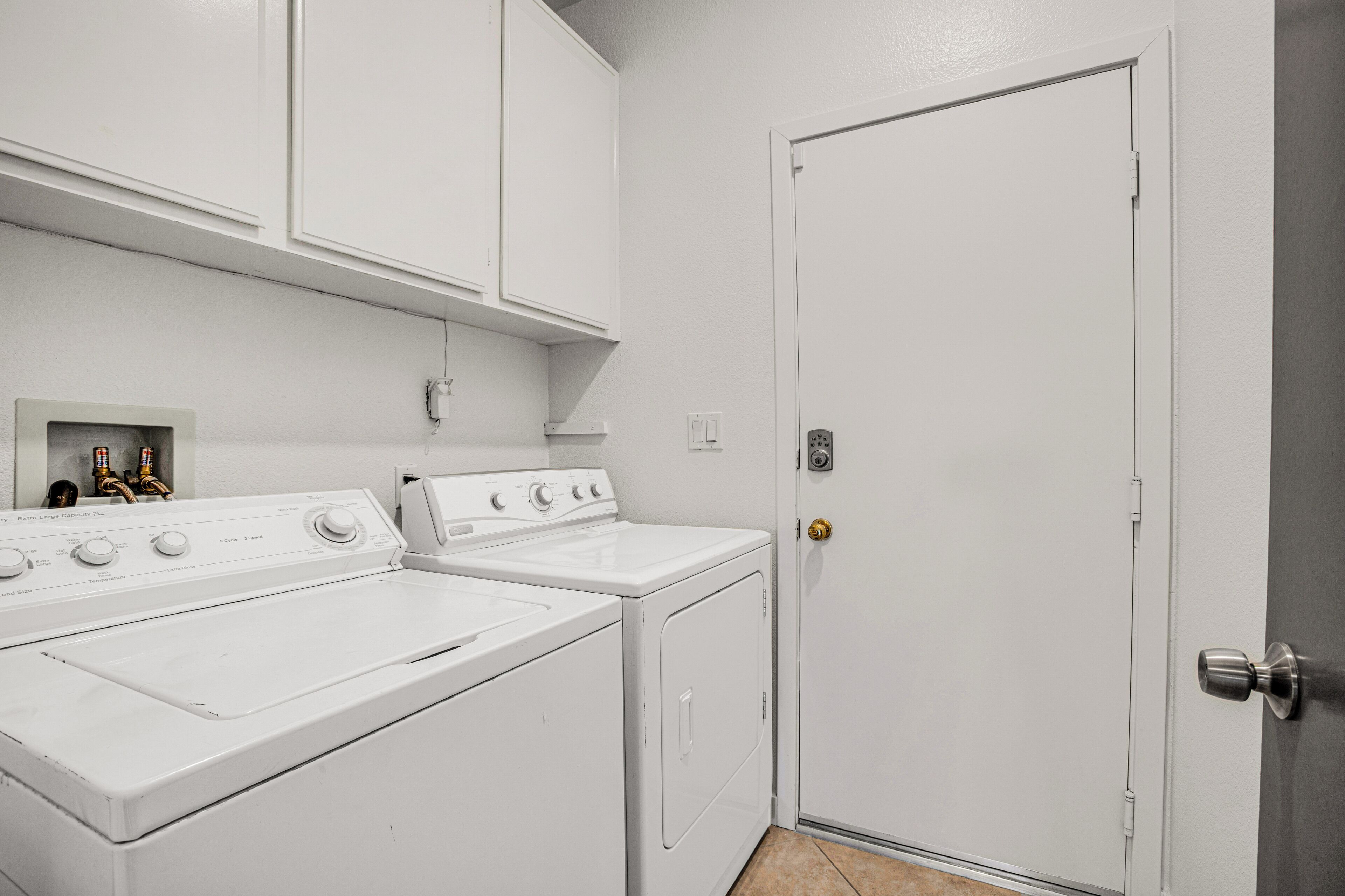 A laundry area with a washer and dryer, a white door, and a small shelf with bottles.