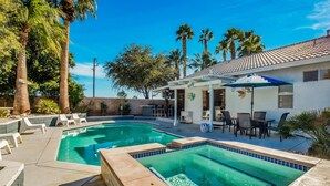 Une piscine entourée d’une terrasse carrelée, de chaises longues et d’un espace extérieur avec des tables et des parasols.