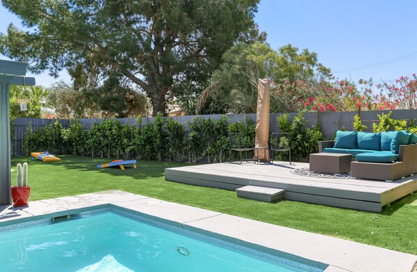 A backyard with a swimming pool, a patio with outdoor furniture, and a variety of plants and trees. - Viminal (Palm Springs)