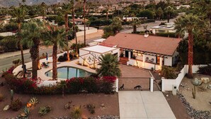 Zona residencial con una casa que tiene piscina, rodeada de palmeras y montañas al fondo.