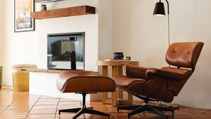 Una sala de estar moderna con un sofá de cuero marrón, un reposapiés a juego, una mesa de centro de madera y una lámpara de pie.