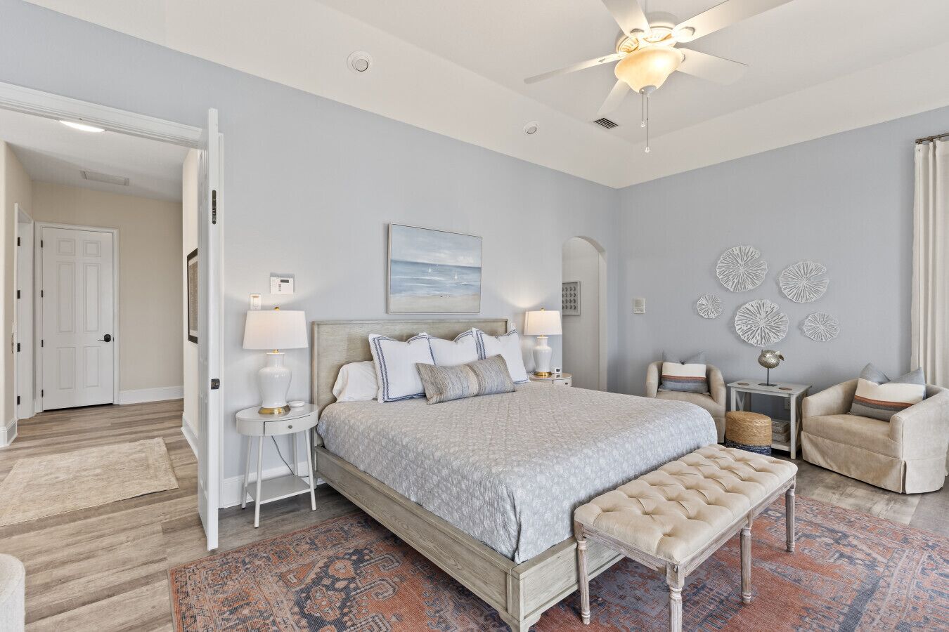 A bedroom with a large bed, bedside tables, a bench, a ceiling fan, and decorative wall art.