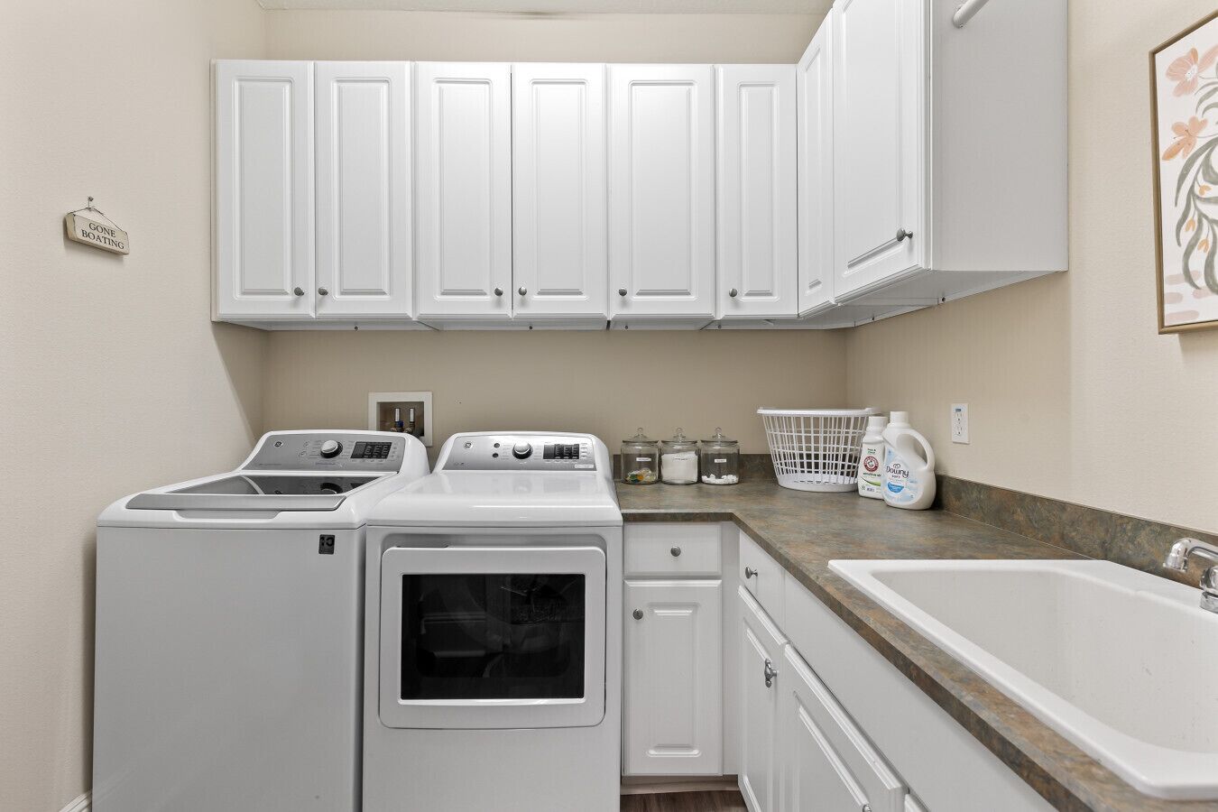 A laundry room with two washing machines, a dryer, a sink, and a countertop with laundry supplies.