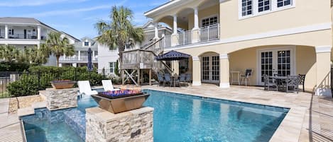 A swimming pool with stone steps, lounge chairs, and a fire pit.