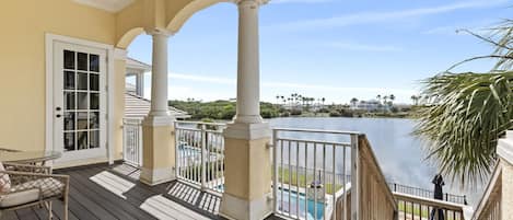 A covered deck with a view of a lake, a pool, and a chair.