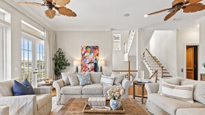 Un salon spacieux avec un plafond haut, une grande fenêtre, un escalier et un ventilateur de plafond.