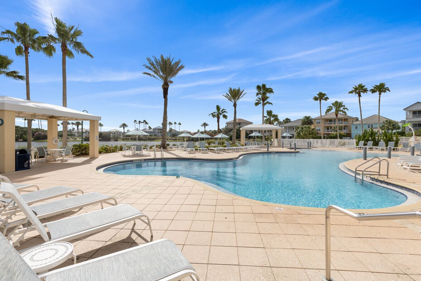 A pool area with lounge chairs, palm trees, and a clear sky.