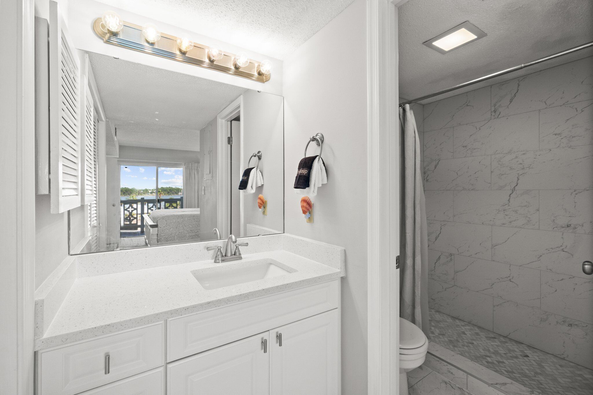 A bathroom with a large mirror, a white sink, and a shower area with marble tiles.