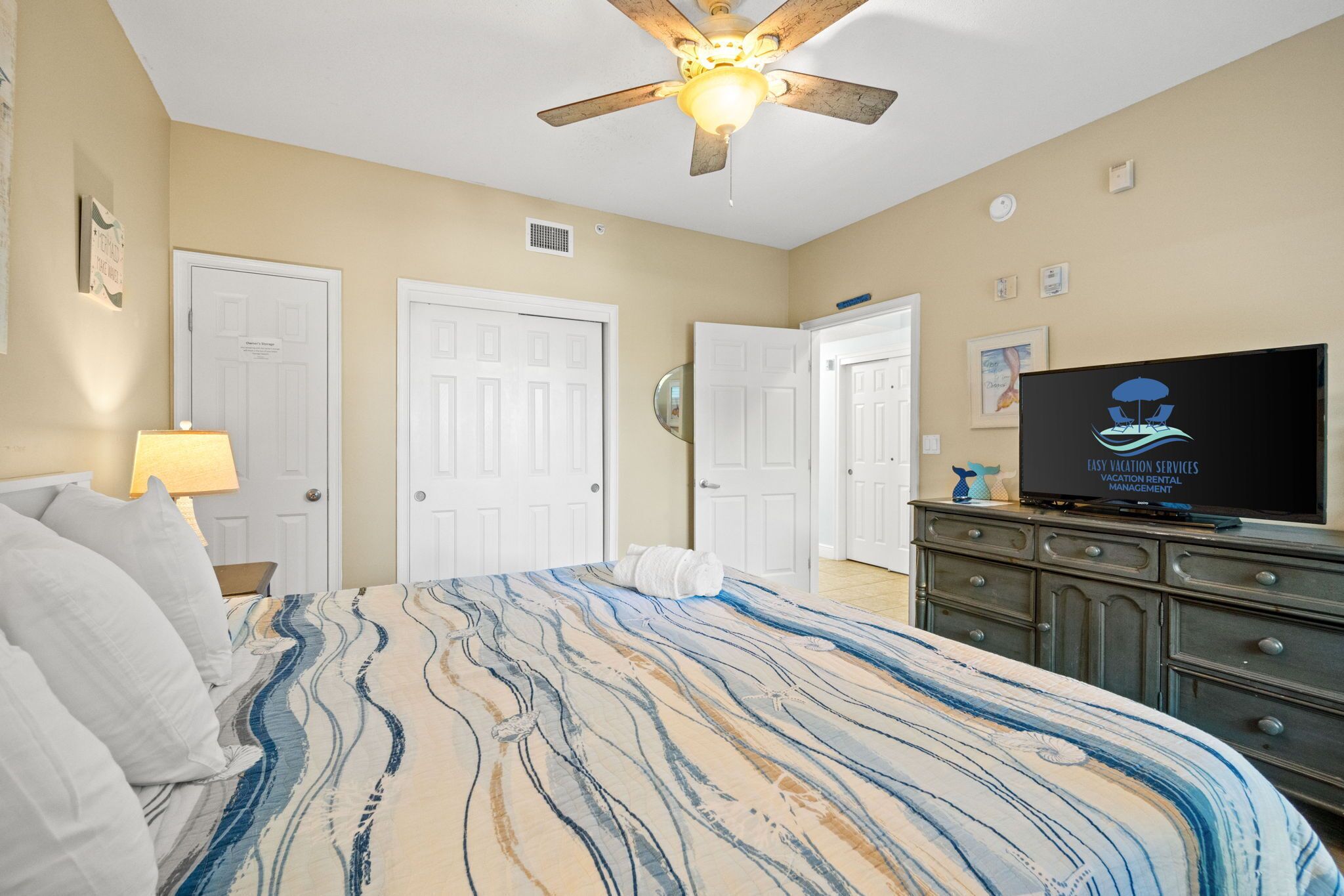 A hotel room with a bed, a ceiling fan, a television, and a dresser.