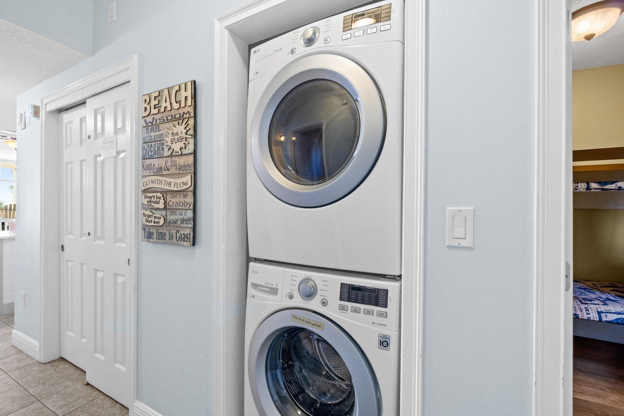 A laundry room with two stacked front-loading washing machines and a wall-mounted sign with motivational phrases.