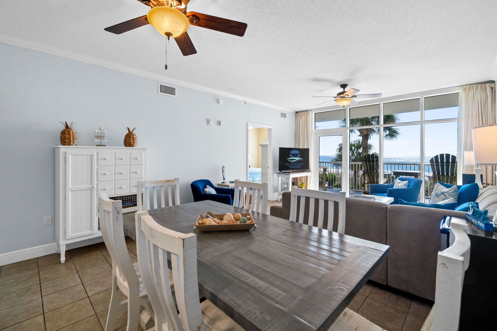 A spacious living area with a dining table, white cabinets, and a large window offering a view of the ocean.
