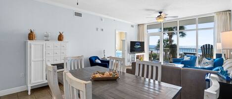 A spacious living area with a dining table, white cabinets, and a large window offering a view of the ocean.