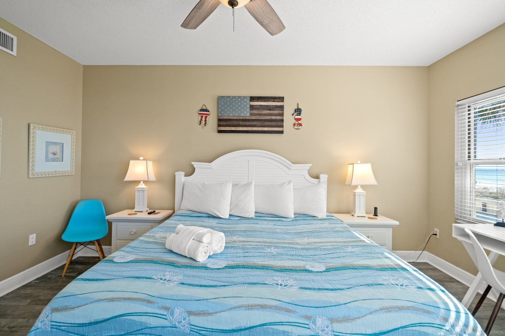 A hotel room with a bed, two bedside tables with lamps, a desk, a chair, and a ceiling fan.