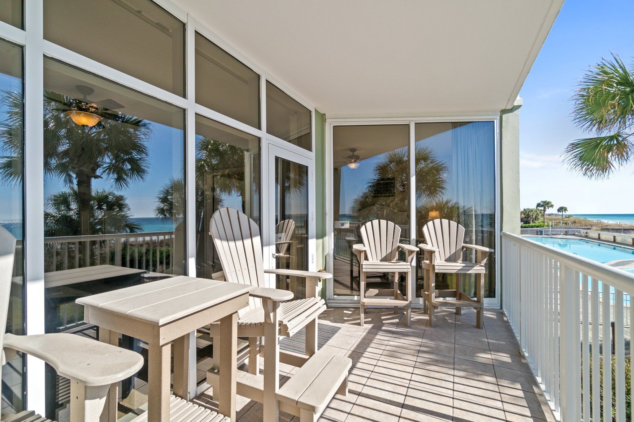Un balcon avec une piscine, des chaises blanches et une table.