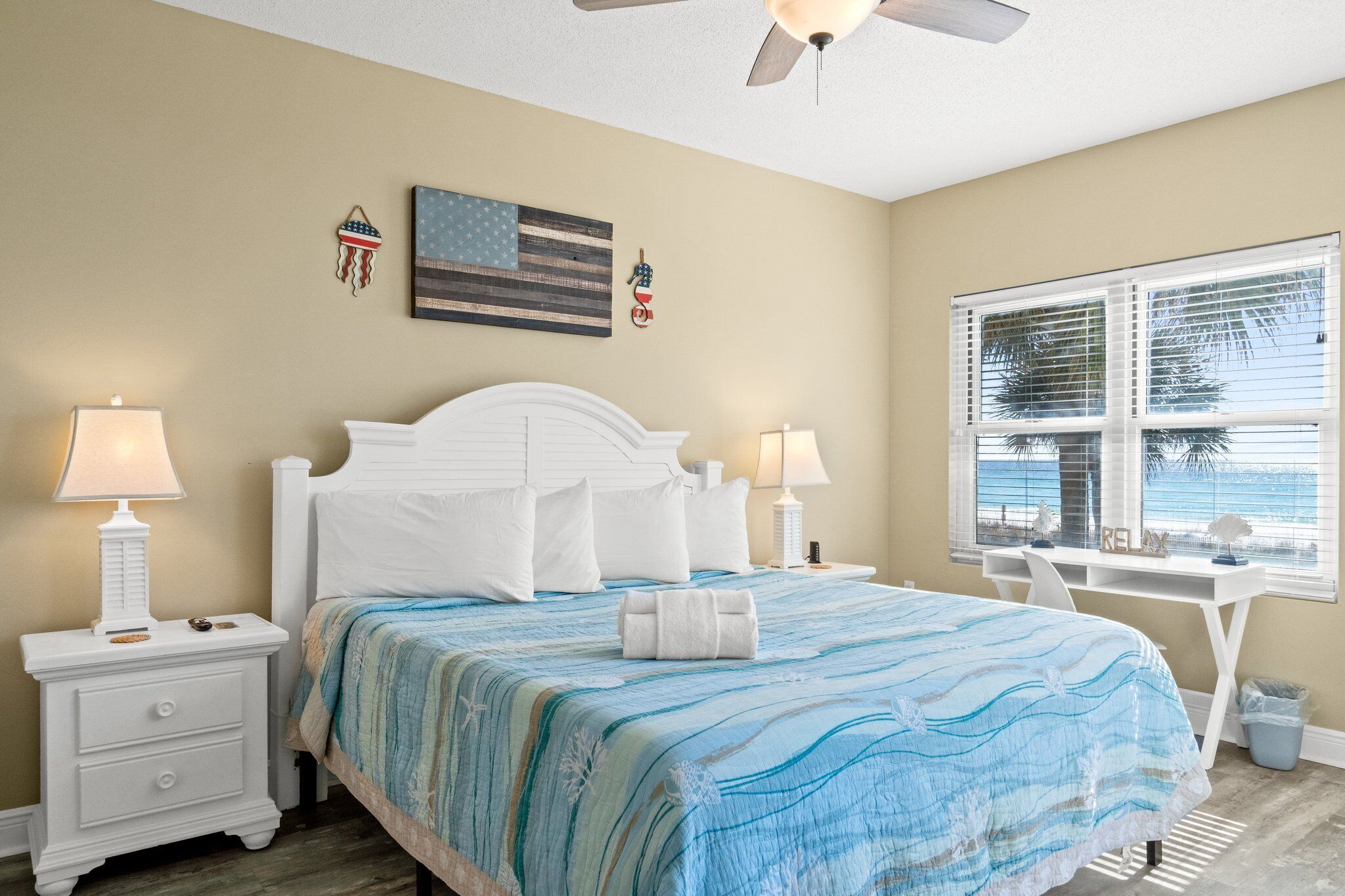 A bedroom with a bed, two bedside tables with lamps, a desk, and a window with a view.