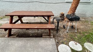 Un montaje para picnic con una mesa de madera y bancos, una mesa redonda pequeña y una parrilla portátil.