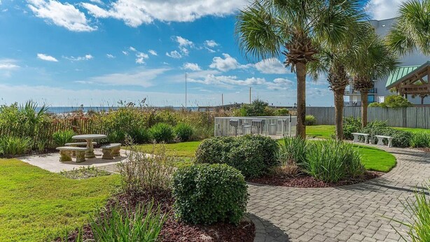 A landscaped outdoor area with a patio, palm trees, and a view of the ocean. - Waters Edge 404 - Okaloosa Dreamin' (Fort Walton Beach)