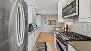 A modern kitchen with stainless steel appliances, white cabinetry, and a tiled backsplash. - Marbella Lane - Chic Abode w Mountain Skyline (Pacifica)