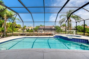 A swimming pool with a glass enclosure, surrounded by palm trees and houses. - Life's Porpoises - 29 Coconut Ct (Palm Coast)