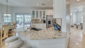 A modern kitchen with granite countertops, stainless steel appliances, and a dining area with wooden chairs and a chandelier. - Life's Porpoises - 29 Coconut Ct (Palm Coast)