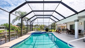 A covered swimming pool with a clear view of the surrounding landscape, including palm trees and neighboring houses. - Life's Porpoises - 29 Coconut Ct (Palm Coast)