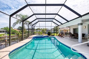 Una piscina cubierta con cerramiento de vidrio, un área de patio con sillas y vistas del vecindario circundante.