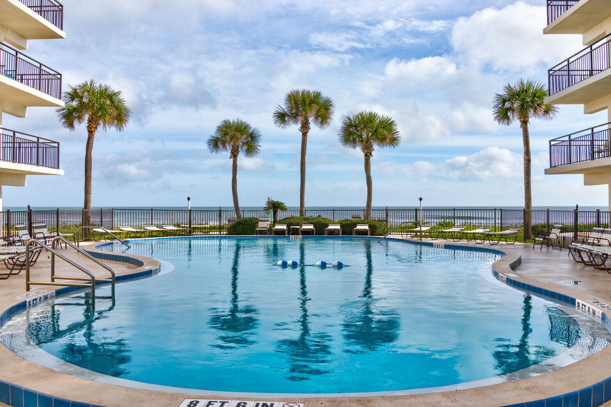 A swimming pool with palm trees, lounge chairs, and a view of the ocean.