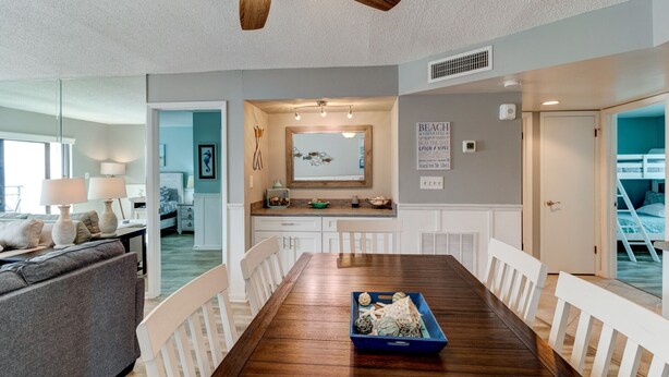 A dining area with a wooden table, white chairs, and a blue tray with decorative items. - Sunny Ormond Beach SOB Condo, Pool, No Drive Beach (Ormond Beach)
