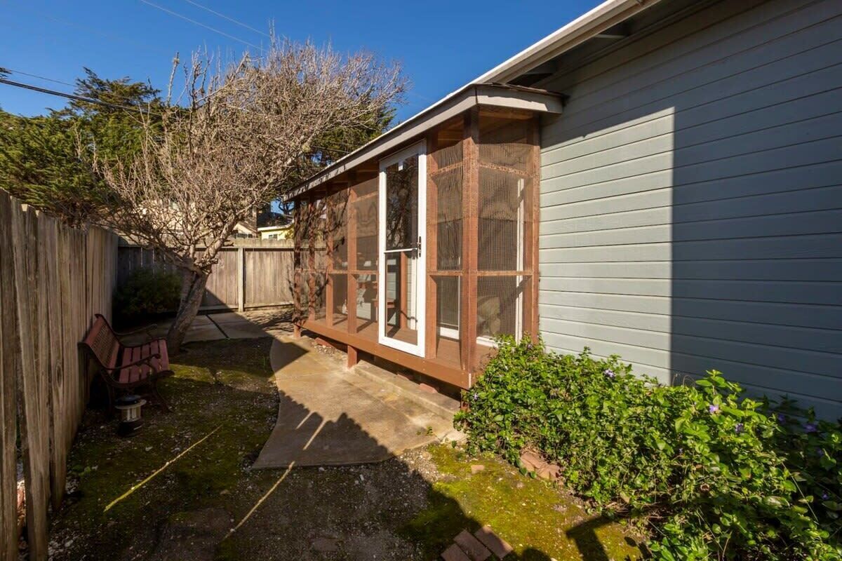 A residential backyard with a wooden fence, a bench, a small garden, and a house with a screened porch.