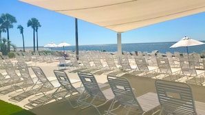Ein Strandloungebereich mit Reihen weißer Liegestühle und Sonnenschirmen mit Blick auf den Ozean.