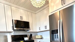A kitchen with white cabinets, a stainless steel refrigerator, a microwave, and a glass of water with lemon slices on a granite countertop. - 2109 Landfall Way (Seabrook Island)