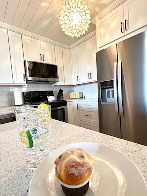 A kitchen with white cabinets, a stainless steel refrigerator, a microwave, and a glass of water with a lemon slice. - 2109 Landfall Way (Seabrook Island)