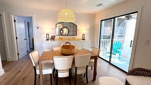 A dining area with a wooden table, white chairs, a wicker basket, and a hanging light fixture. - 2109 Landfall Way (Seabrook Island)