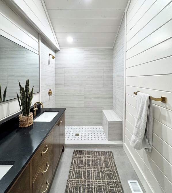 A bathroom with a vanity, a mirror, a shower, and a towel rack.
