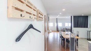 Ett modernt hotellrum med en trähylla som är monterad på väggen och där det står ”HÄR ÄR DET SKÖNT ATT VARA”, en svart galge, en matplats med ett bord och stolar samt ett stort fönster med gardiner.