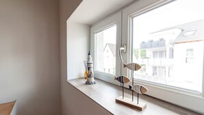 Ett rum med ett stort fönster, ett litet bord med dekorativa föremål och utsikt över de omkringliggande byggnaderna.
