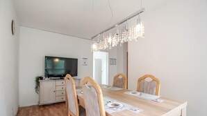 Ein Essbereich mit einem Holztisch, vier Stühlen, einem Fernseher auf einem Schrank und einer Kronleuchter.