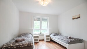 Ein kleiner, heller Raum mit zwei Einzelbetten, einem Fenster und einer Deckenleuchte.