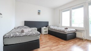 Ein modernes Schlafzimmer mit zwei Betten, einer weißen Wand und einem großen Fenster.