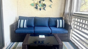 A dark blue sofa with striped pillows, a glass-top coffee table, and a wall-mounted decorative fish wall art. - 2013 Long Bend Drive (Seabrook Island)