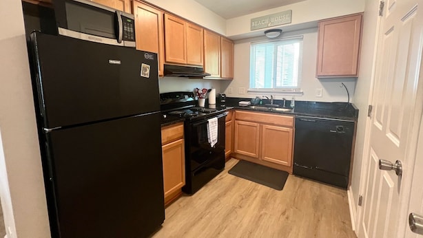A compact kitchen with wooden cabinets, a black refrigerator, a microwave, a stove, and a dishwasher. - 2013 Long Bend Drive (Seabrook Island)