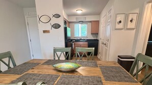 A dining area with a wooden table, green chairs, and a colorful bowl. There are wall decorations and a kitchen in the background. - 2013 Long Bend Drive (Seabrook Island)