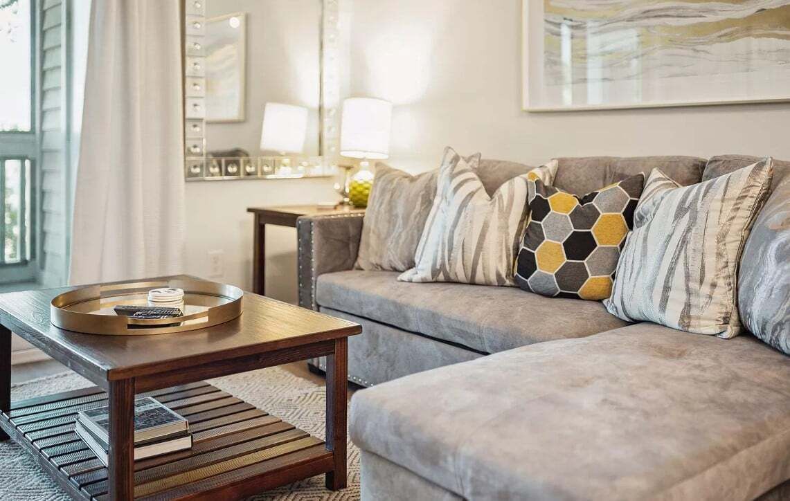 Ein Wohnzimmer mit einem grauen Sofa, einem Holztisch und einer Ablage mit Büchern.