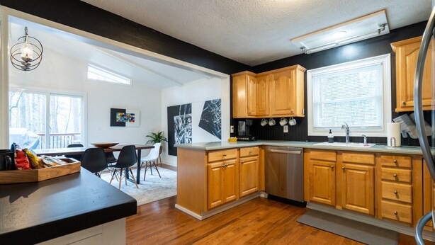 A modern kitchen with wooden cabinets, a black countertop, and a dining area with a table and chairs. - 306 Jason Court, Woodstock (Woodstock)