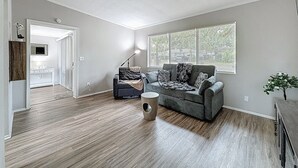 A living room with a grey couch, a coffee table, and a large window with blinds. - 3012 E Norfolk Street (Tampa)