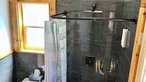 A modern bathroom with a toilet, shower, and a window.